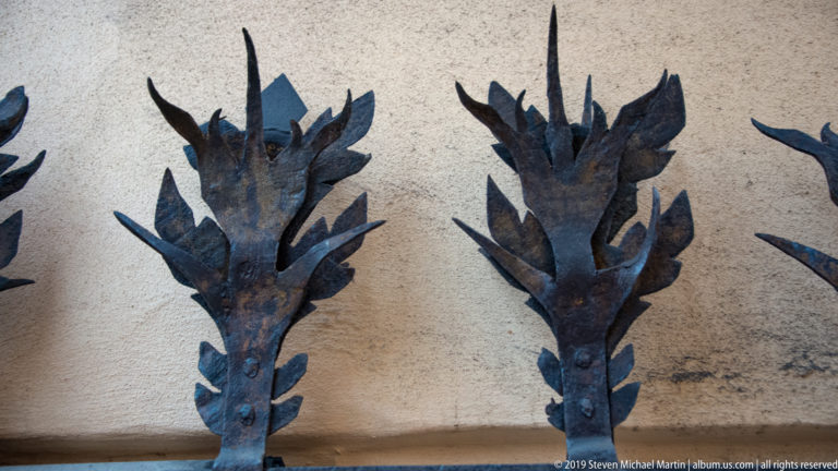 Close view of repeated dark wrought-iron leaf clusters mounted against a pale textured wall.