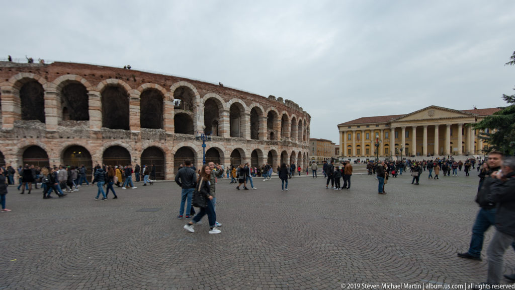 Arena di Verona at left and columned Palazzo Barbieri at right across crowded Piazza Bra.
