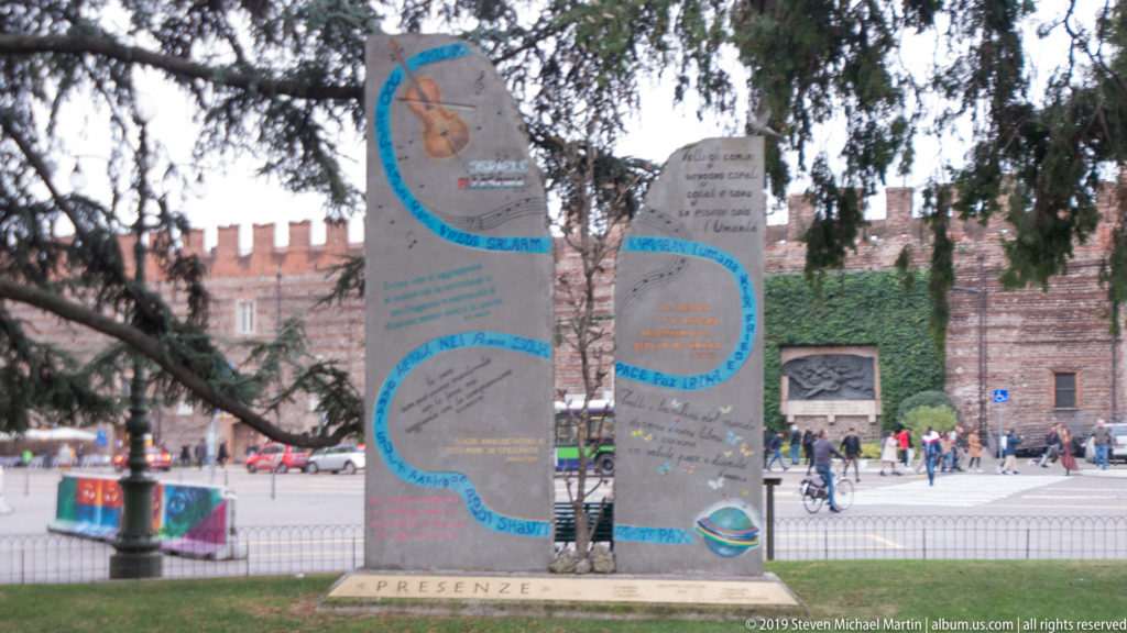Two irregular inscribed slabs of the Presenze peace monument in Piazza Bra, with a small tree between them.