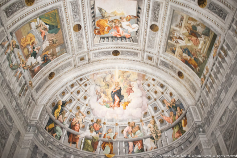 Wide upward view of the painted apse, combining the central semi-dome frescoes with rectangular narrative panels across the adjoining vault.
