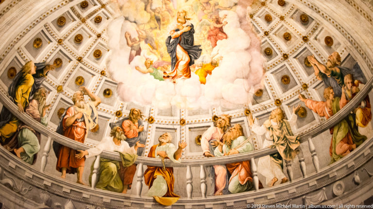 Broad view of the apse frescoes, with a central figure in clouds above a semicircle of monumental sacred figures and decorated coffering.