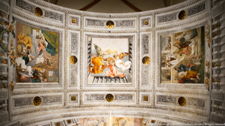 Three rectangular religious fresco panels set in the curved apse ceiling, separated by pale decorative coffering and round medallions.