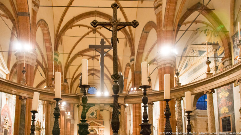 Tall crucifix above the sanctuary rail and candlesticks, with brick piers and ribbed cathedral vaults extending into the background.