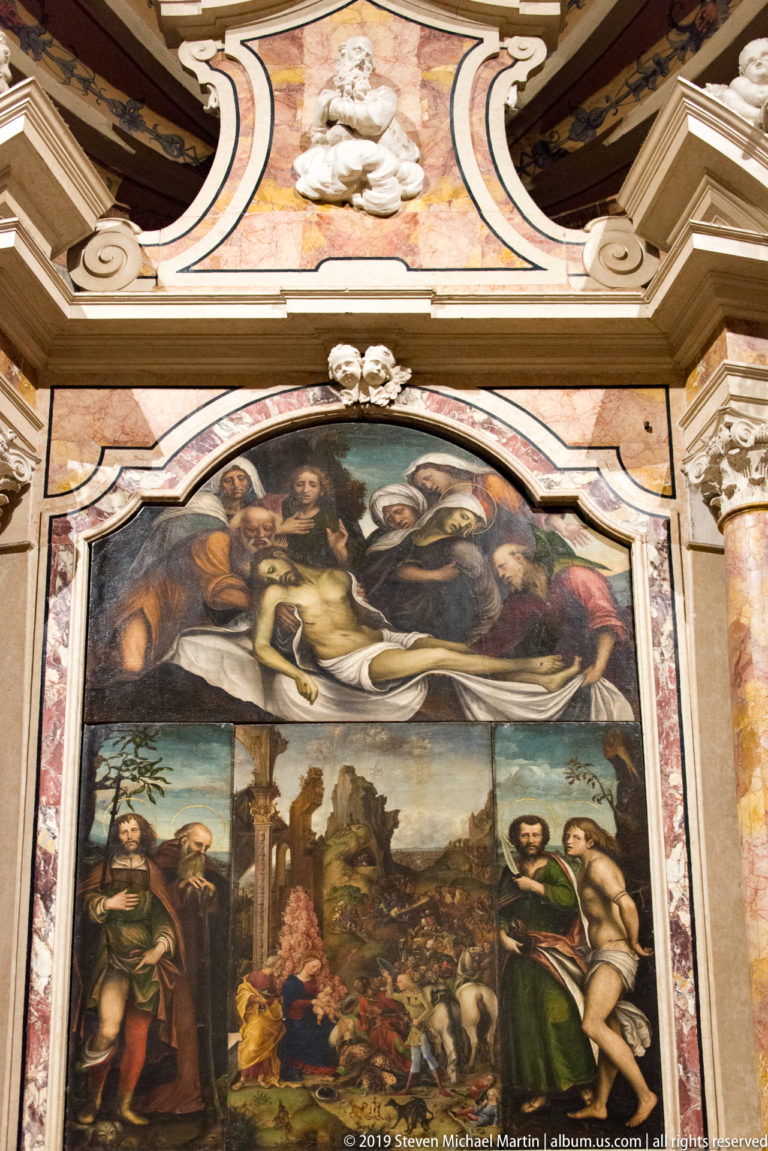 Large two-part religious altarpiece with crowded upper scene and standing figures in a landscape below, enclosed by ornate polychrome framing.