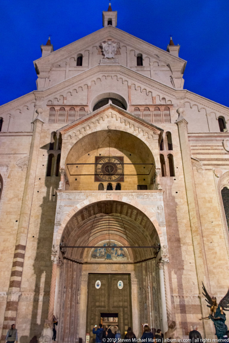 Low-angle close view of Verona Cathedral’s west entrance, showing the recessed arch, projecting porch, striped masonry, and upper façade.