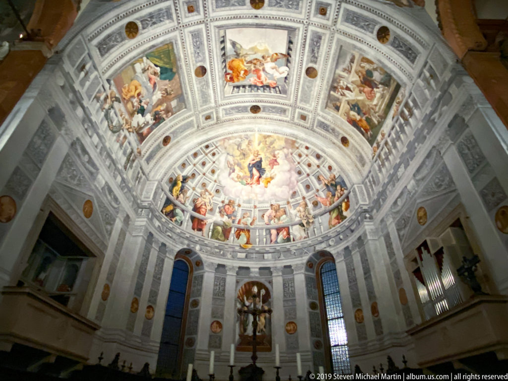 Frescoed semi-dome above the cathedral choir, with a central heavenly scene, surrounding figures, decorative coffering, and tall windows below.