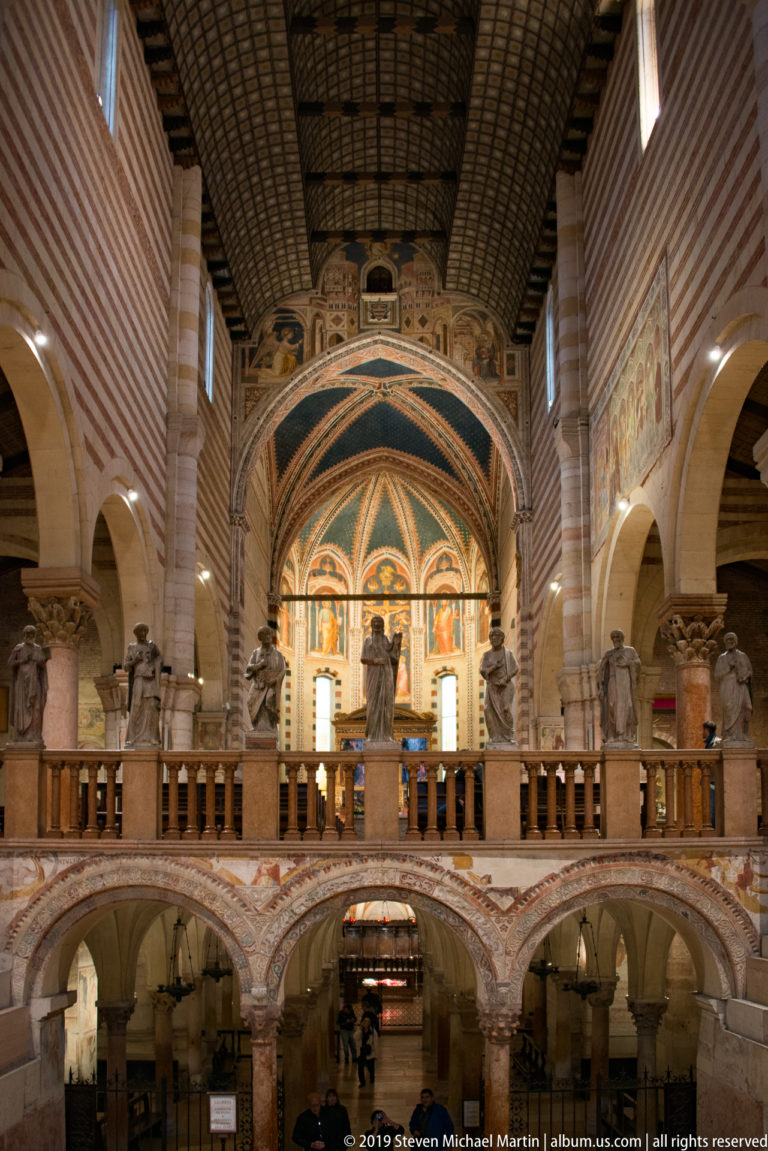 Wide interior view toward the raised choir, statues, crypt openings, and richly painted apse.