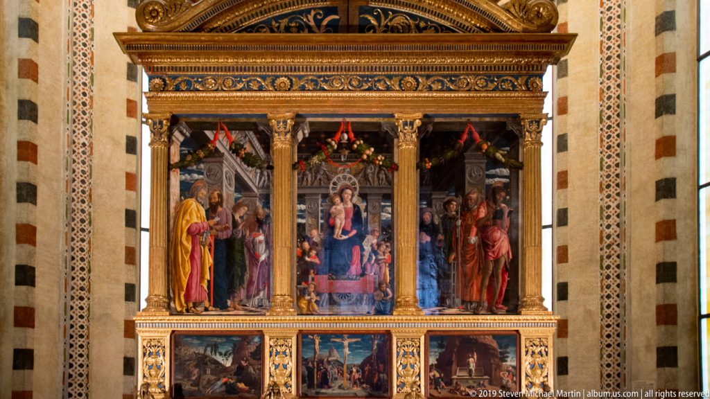 Large framed Renaissance altarpiece with enthroned Virgin and Child, flanking saints, and predella scenes below.