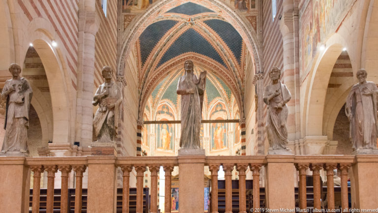 Central stone statues on a balustrade before the richly painted apse of San Zeno.