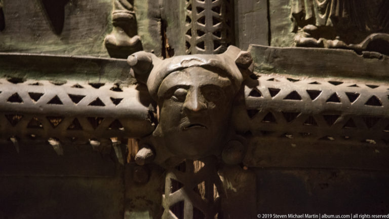 Close-up of a cast bronze human head projecting from patterned metalwork on the church doors.