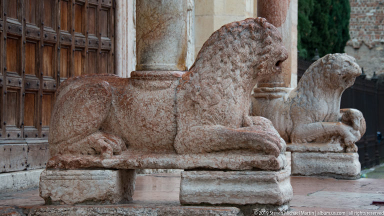 Two weathered stone lion sculptures aligned beside the west doorway, each crouching on a low plinth.
