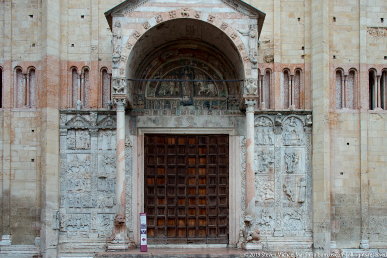 Front view of San Zeno’s main doorway with bronze-panel doors, carved side reliefs, columns, and painted tympanum.