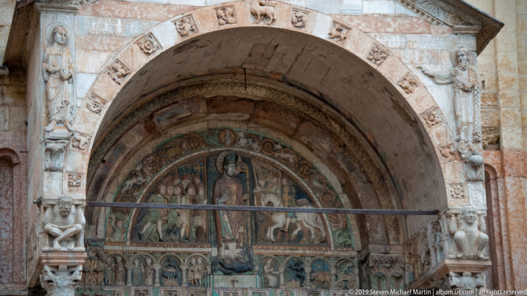 Arched portal tympanum with a central painted sacred figure, smaller figures, and carved stone framing.