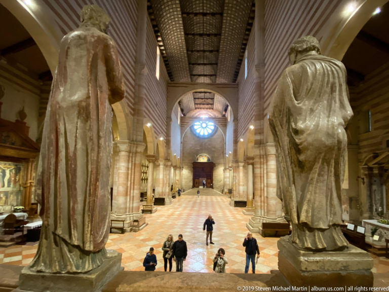 View from the raised sanctuary down the long nave toward the west rose window, with large stone statues in front.