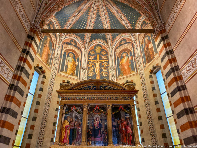 Painted sanctuary with a triptych-style altarpiece below frescoed walls and a richly colored ribbed vault.