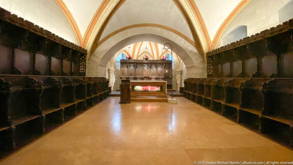 Narrow vaulted choir with dark wooden stalls on both sides and an altar at the far end.