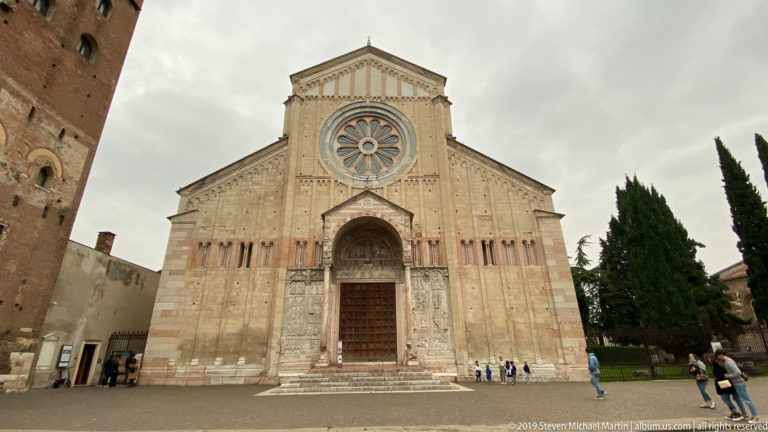 Front view of the basilica façade with large wheel window, projecting porch, carved doorway, and patterned masonry.