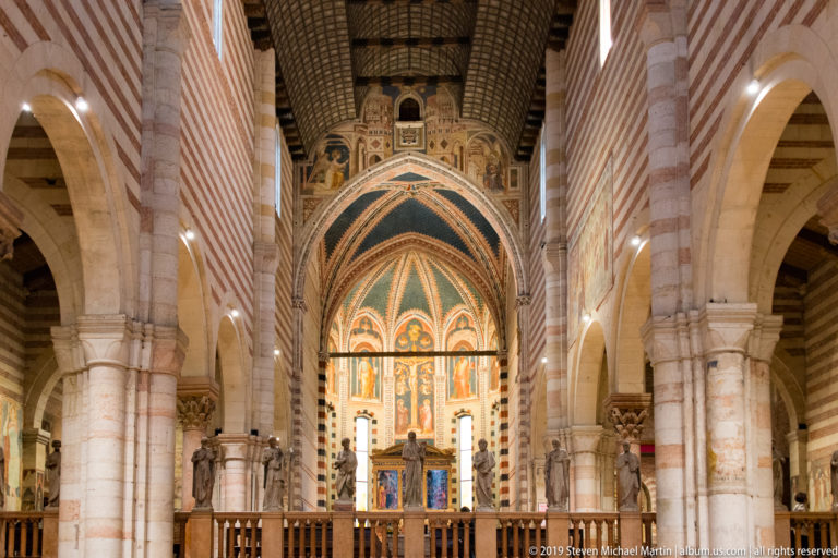 Vertical view of the painted apse framed by striped piers, with statues along the choir balustrade.