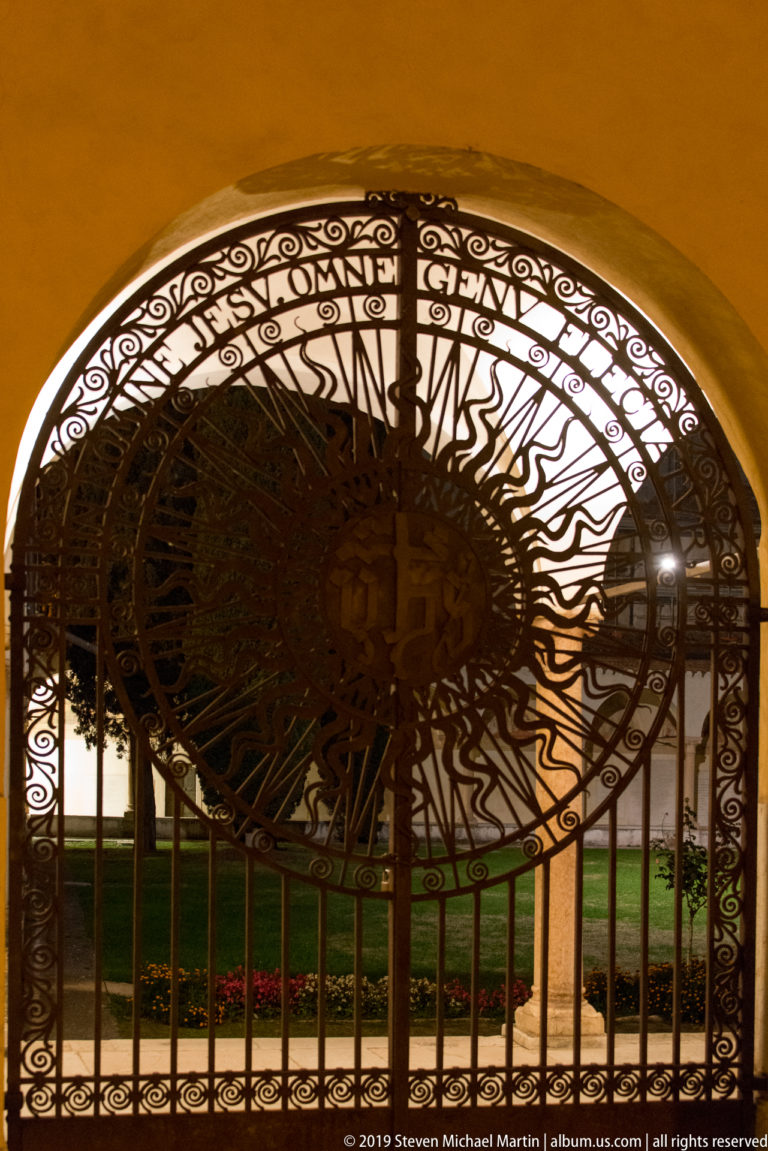Large circular wrought-iron screen filling an archway, with dense radial bars and curling ornament silhouetted by backlighting.