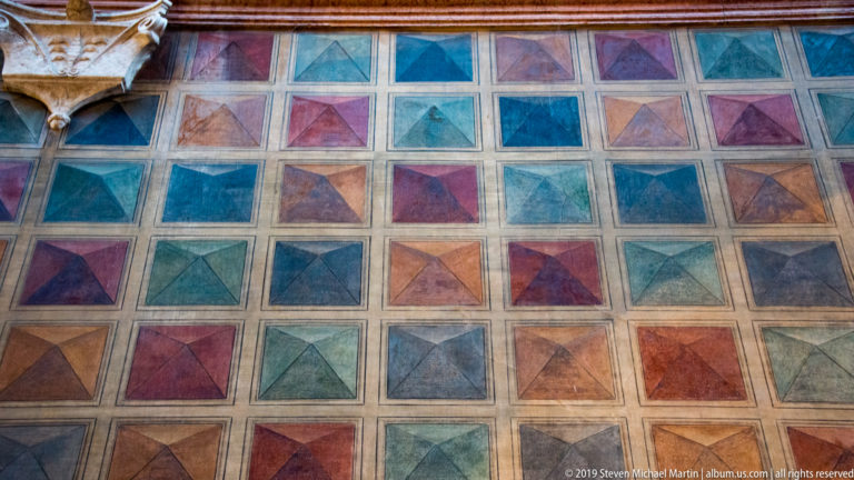 Grid of square pavement panels divided into multicolored triangular sections in red, blue, green, ocher, and violet.