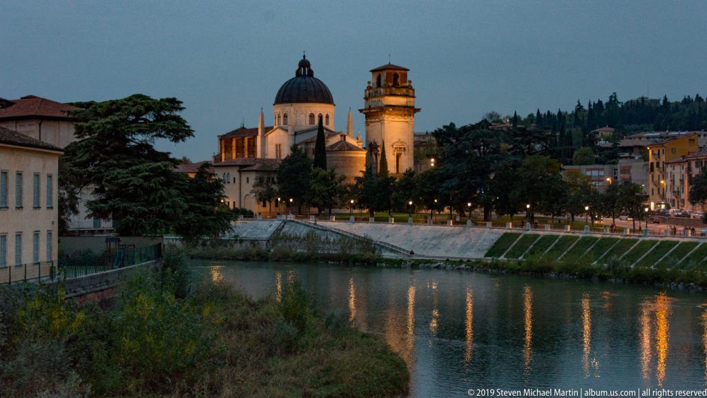 Blue-hour view of San Giorgio in Braida and its campanile across the Adige, with dark trees and scattered river reflections.