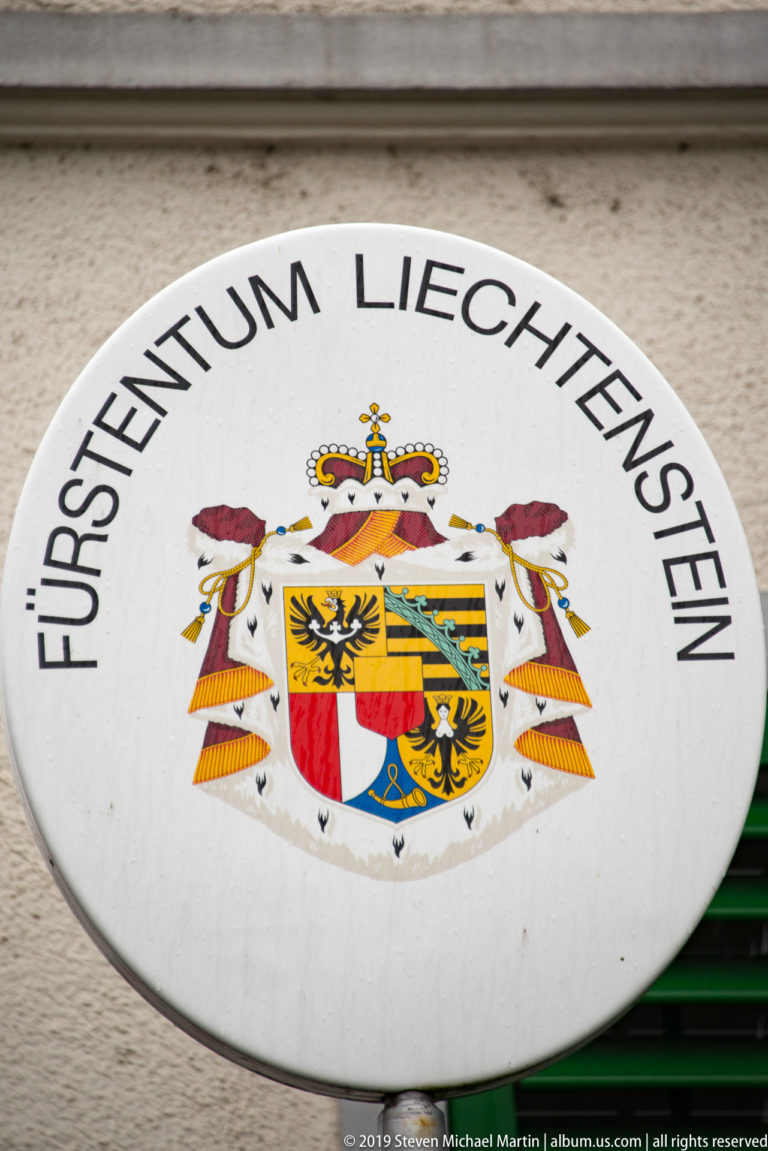 Circular Fürstentum Liechtenstein sign with the principality’s crowned multicolored coat of arms centered beneath black lettering.