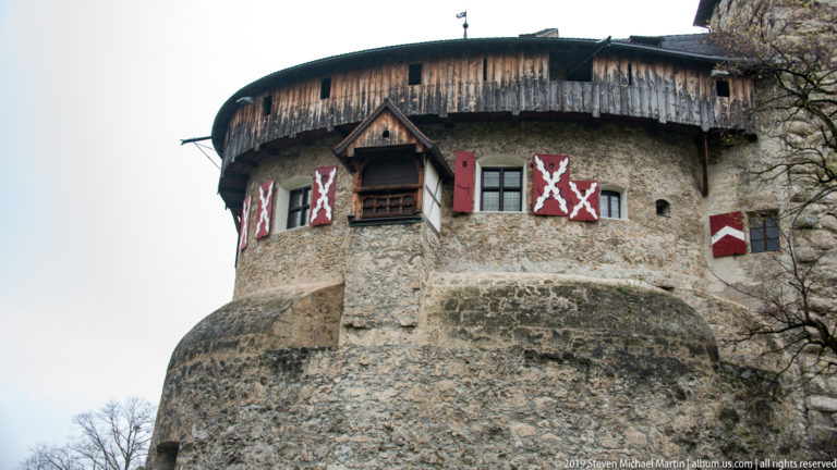 Close low-angle view of Vaduz Castle’s round stone tower with timber upper gallery and painted shutters.