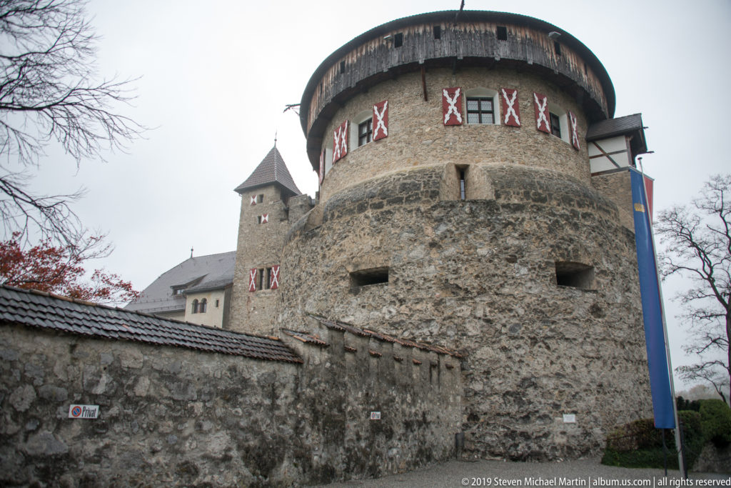 Low-angle view of Vaduz Castle’s round stone tower with timber gallery and red-and-white shutters.