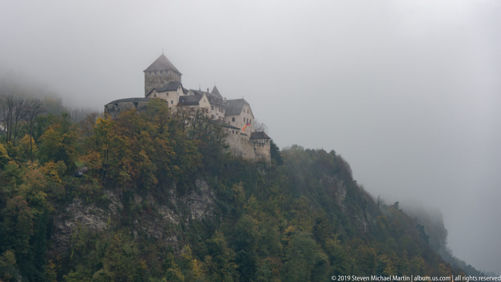 Vaduz Castle on a steep wooded ridge, partly veiled by fog and low cloud.