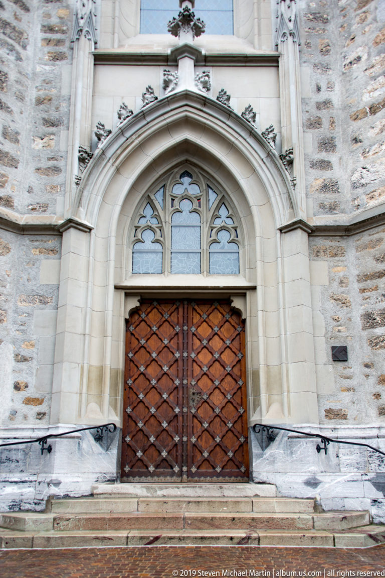Pointed stone church portal with tracery windows, wooden double doors, and broad entrance steps.
