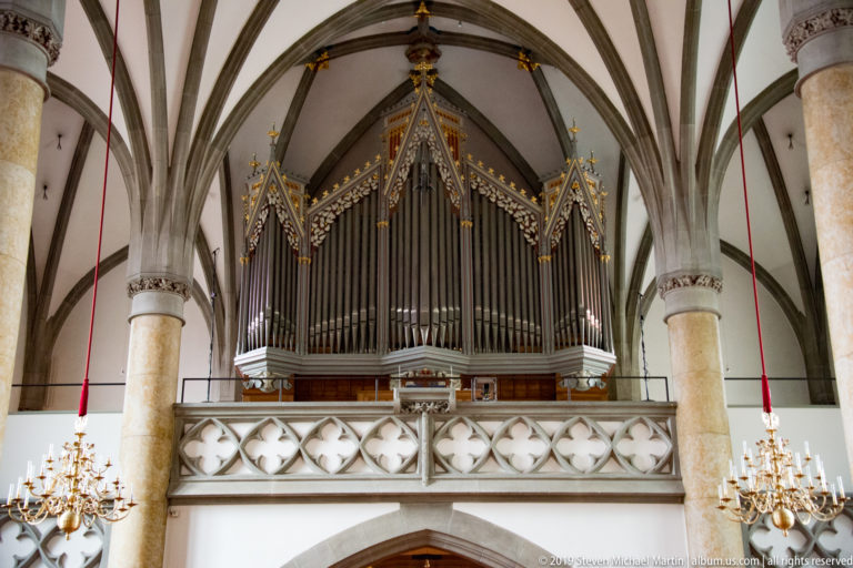 Large pipe organ with pointed Gothic-style cases above a pierced stone gallery between tall columns and ribbed vaults.