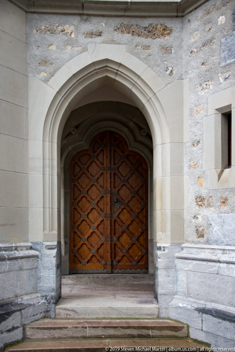 Pointed Gothic stone portal with layered moldings and dark double wooden doors patterned with diagonal panels.