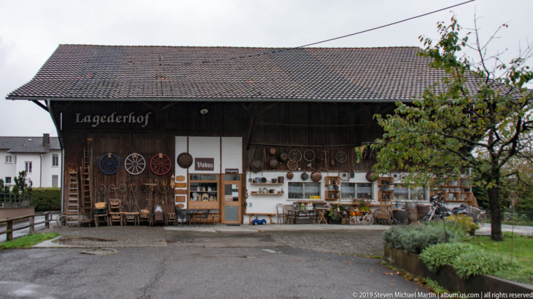 Wide view of the timber Lagederhof with rural tools and objects displayed across the façade beside a fruit tree.