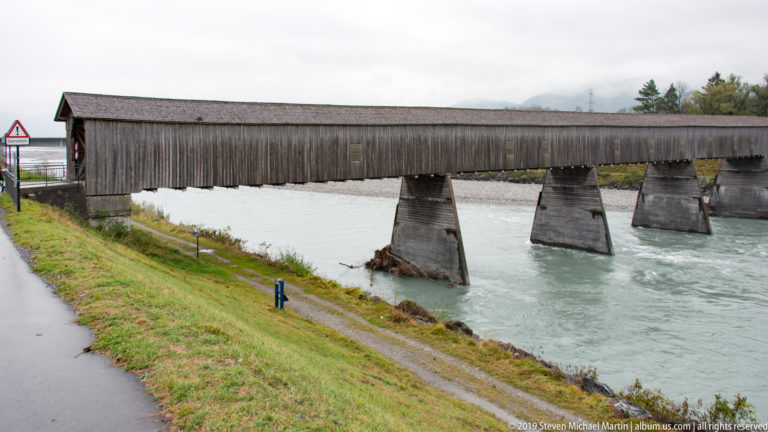 Long covered wooden Old Rhine Bridge crossing the river on heavy piers between Vaduz and Sevelen.
