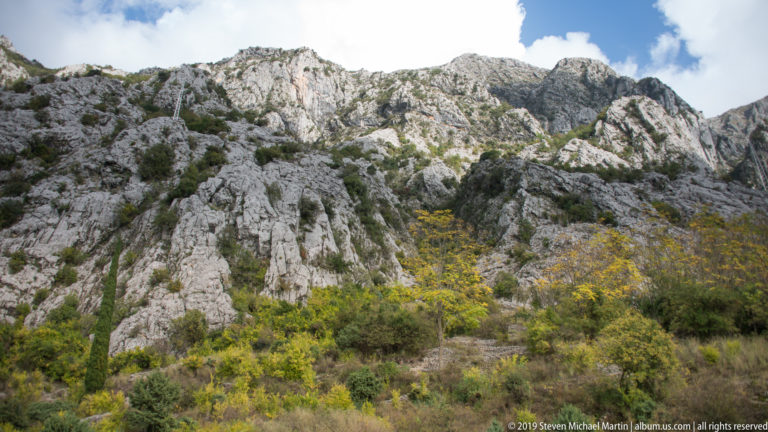 Rugged pale limestone cliffs above yellowing autumn woodland and scrub on a steep mountain slope in Montenegro.