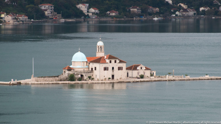 Our Lady of the Rocks church with pale blue dome and bell tower on a low island in the Bay of Kotor.