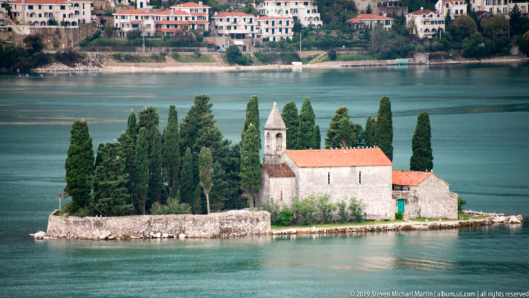 Stone church with red tile roof and tall cypress trees on Saint George Island in the Bay of Kotor.