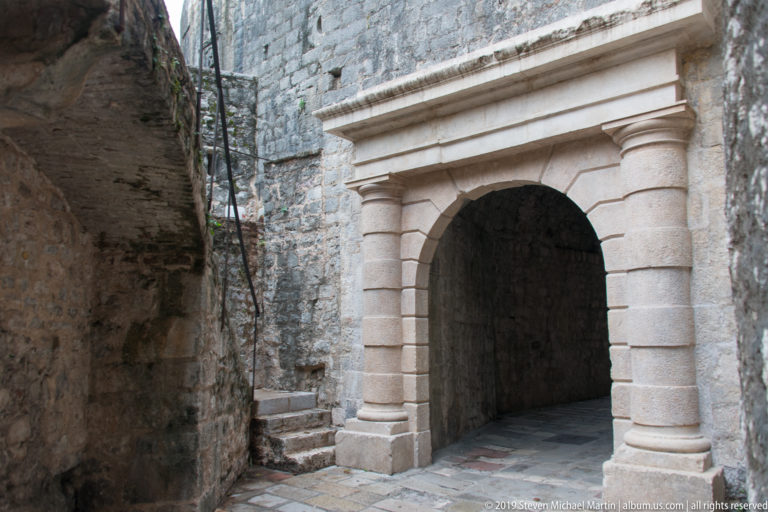 Formal rounded stone portal with pilasters and molded cornice set into rough fortified masonry in Kotor.