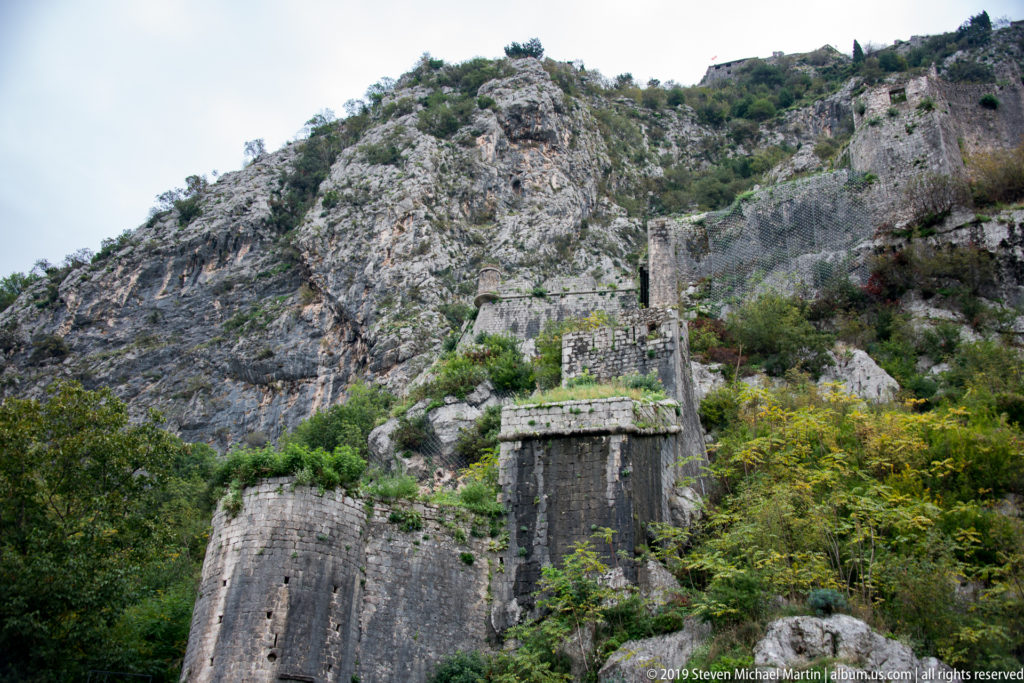 Multiple tiers of stone fortifications ascending a rugged mountain slope above Kotor.