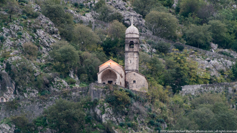 Small stone church and slender bell tower set on a steep rocky hillside above Kotor.