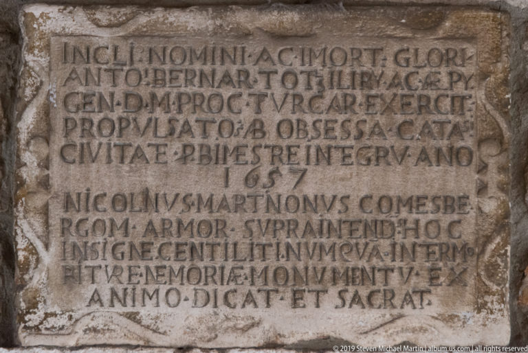 Weathered rectangular stone panel covered with multiple lines of carved Latin capital letters in Kotor.
