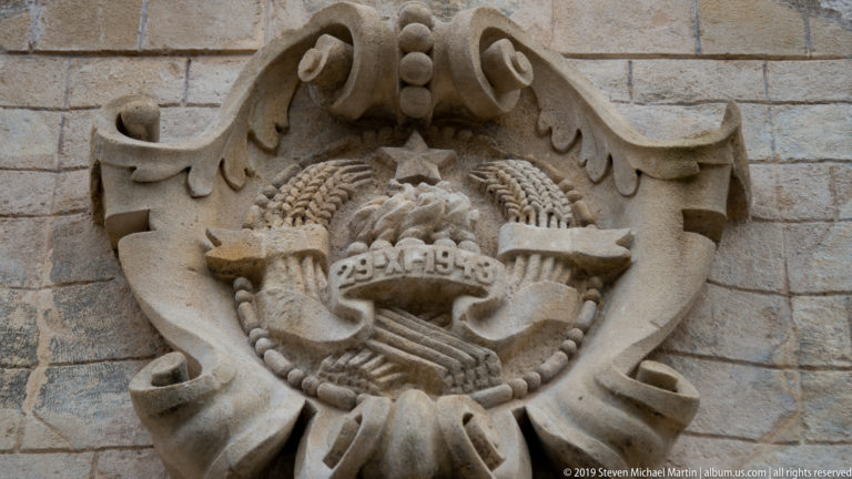 Elaborate carved stone coat of arms with scrolling foliage and a central shield mounted on a rusticated wall in Kotor.