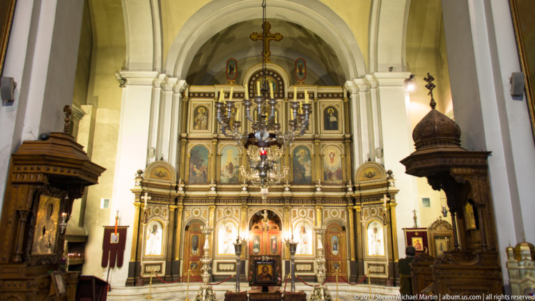 Wide interior view of St. Nicholas Church looking down the nave toward the iconostasis beneath tall white arches.