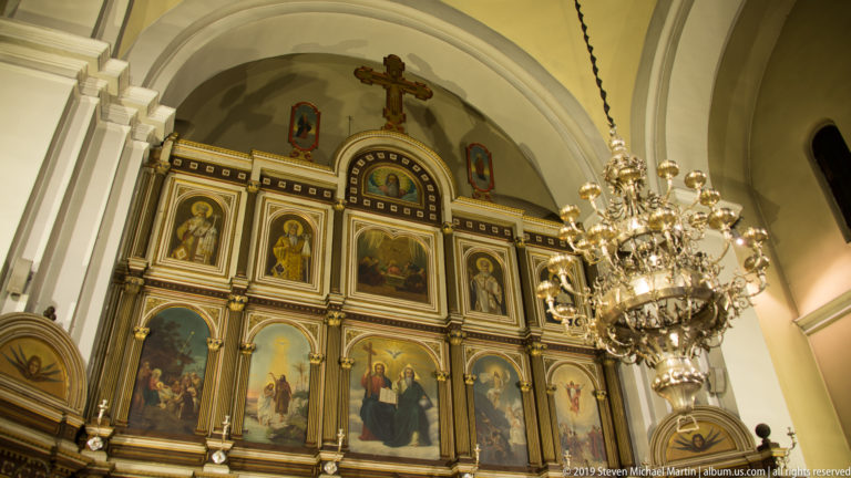 Large metal chandelier suspended before the upper tiers of the painted iconostasis in St. Nicholas Church, Kotor.