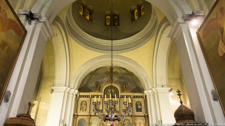 Interior of St. Nicholas Church in Kotor looking toward the painted iconostasis beneath white arches and a central dome.