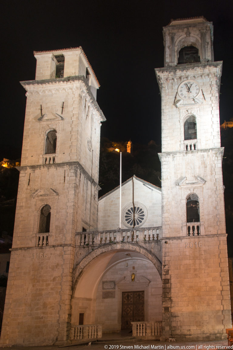 Illuminated twin-towered façade of the Cathedral of Saint Tryphon with rose window and arched entrance at night in Kotor.