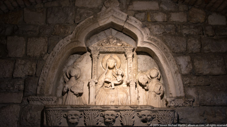 Weathered stone relief of the Madonna and Child in a pointed niche with two kneeling figures at the sides.