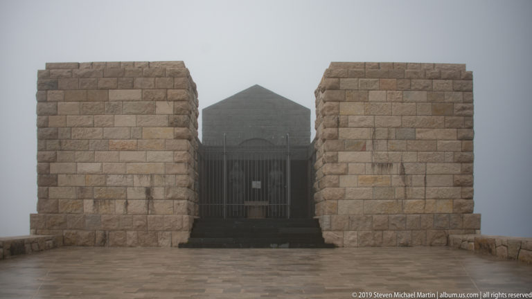 Front view of the Njegoš Mausoleum, with two massive stone pylons framing a dark central entrance in dense fog.
