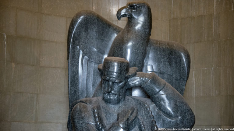 Close view of the seated dark-stone statue of Petar II Petrović-Njegoš with a monumental eagle rising behind him.