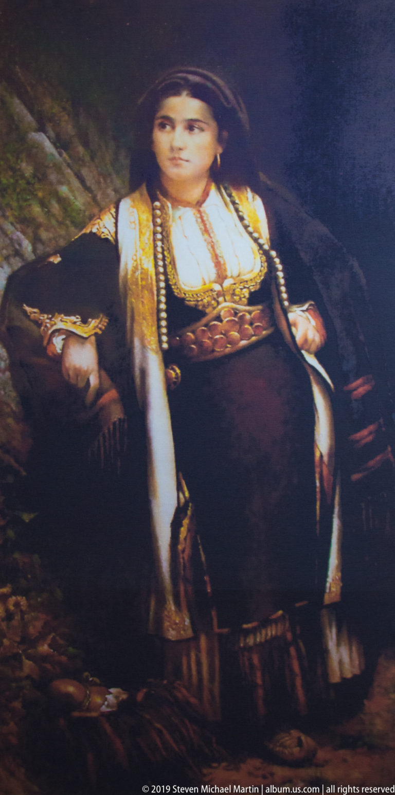 Painted portrait of a seated young woman wearing an embroidered vest, white blouse, jewelry, and dark traditional dress.